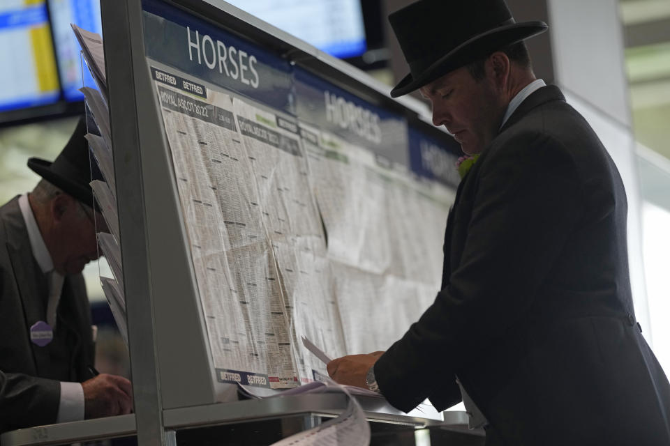 A Racegoer looks at the form guides as he selects his bets near a betting kiosk on the fifth day of the Royal Ascot horserace meeting, at Ascot Racecourse, in Ascot, England, Saturday, June 18, 2022. (AP Photo/Alastair Grant)
