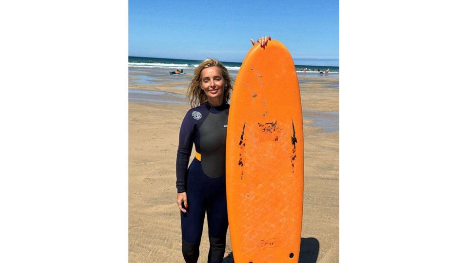 woman standing in wetsuit with surfboard