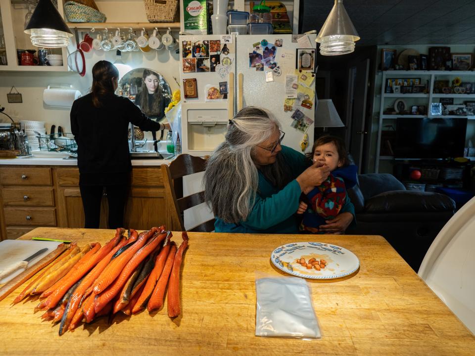 Pam Smith feeds her 20-month-old grandson, Galushia Smith, smoked king salmon—the first of the season—in her home kitchen while her daughter-in-law, Holly Smith, washes her hands in preparation to help process and package it.