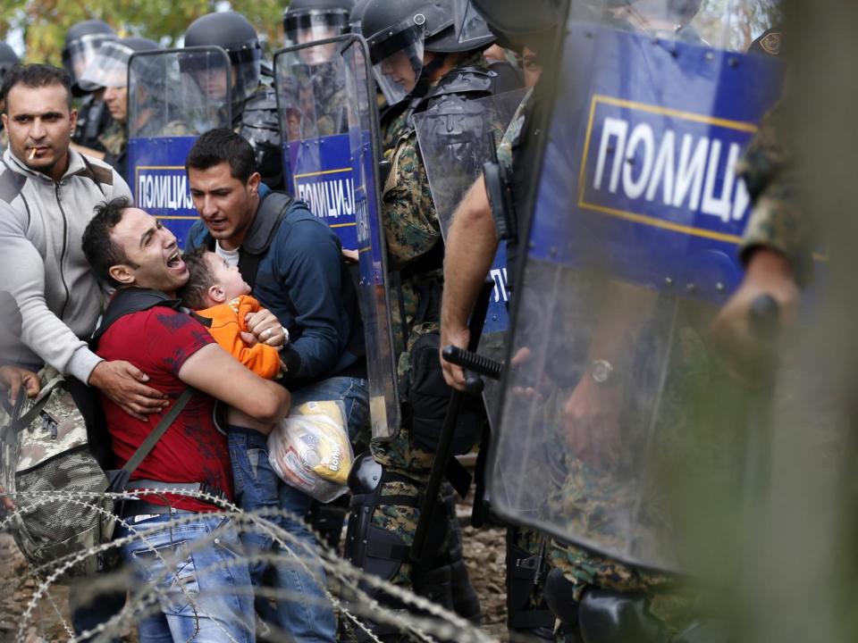 Migrant men help a fellow migrant man holding a boy as they are stuck between Macedonian riot police officers and migrants during a clash near the border train station of Idomeni, (AFP/Getty)