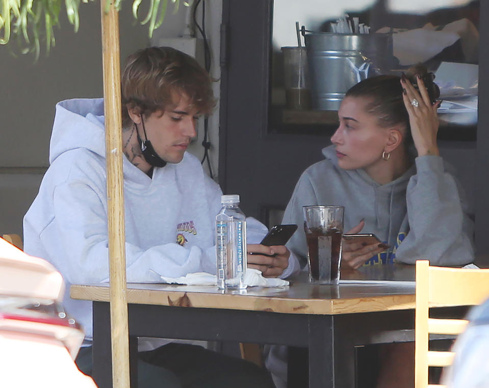 Justin and Hailey looking at their phones while they sit at an outdoor dining table