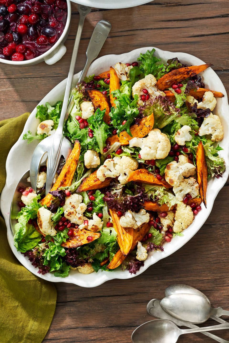 sweet potato and cauliflower salad in a large white oval serving dish with serving utensils