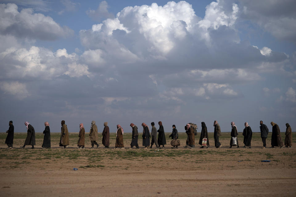 Men walk to be screened after being evacuated out of the last territory held by Islamic State militants, near Baghouz, eastern Syria, Friday, Feb. 22, 2019. (AP Photo/Felipe Dana)