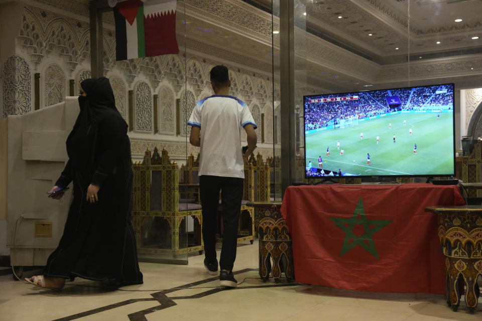 A woman and a server pass near a television showing the World Cup round of 16 soccer match between France and Poland inside Marrakech restaurant, in Doha, Qatar on Sunday Dec. 4, 2022. (AP Photo/Ashley Landis)