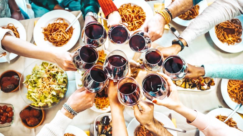 Group clinks red wine glasses over bowls of pasta