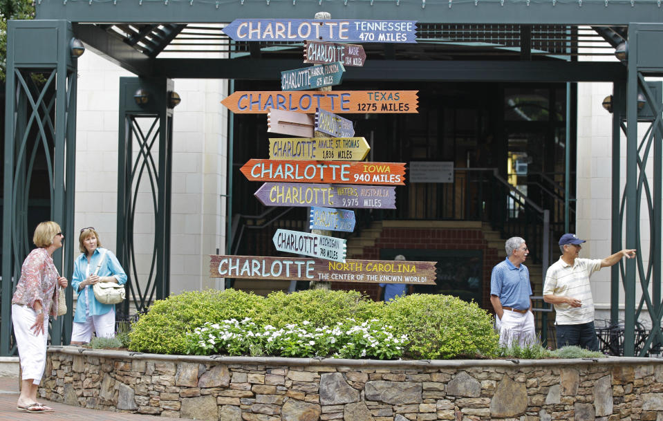This July 17, 2012 photo shows visitors walking past "Charlotte" signs at The Green park in downtown Charlotte, N.C. The Green, a 1.5-acre downtown park at 435 S. Tryon St., is a literary-themed park with sculptures of giant books, pages and a walkway of sounds. Bright signs mark the intersections of author names, including “Emily” and “Bronte,” “Herman” and “Melville,” and “Alice” and “Walker.” (AP Photo/Chuck Burton)