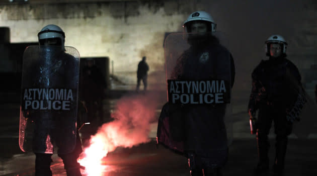 <b>Jan. 28, 2012</b><br><br> <b>Greece reaches a tentative deal with its private creditors to significantly reduce the country's debt, but Germans persist in limiting loans and demanding more austerity cuts.</b><br><br> A riot policeman stands guard in front of the Greek parliament as a flare thrown by protesters burns during a protest in Athens.