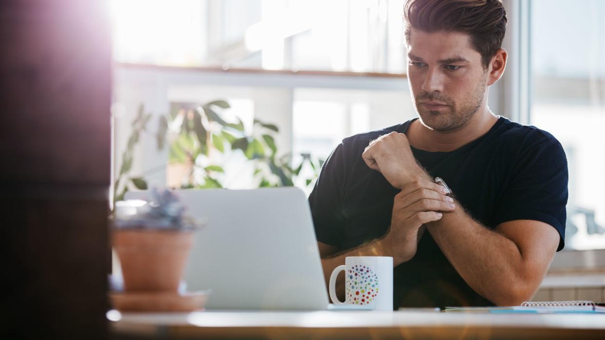 Shot of young man sitting at his desk and looking at a laptop.