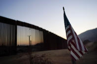 A flag sits just north of a new section of the border structure, behind, Thursday, Sept. 24, 2020, near Tecate, Calif. President Donald Trump’s reshaping of U.S. immigration policy may be most felt in his undoing of asylum. With immigration laws temporarily suspended at the border during the pandemic, people who enter the U.S. illegally are immediately “expelled” without even a piece of paper to record the incident. (AP Photo/Gregory Bull)