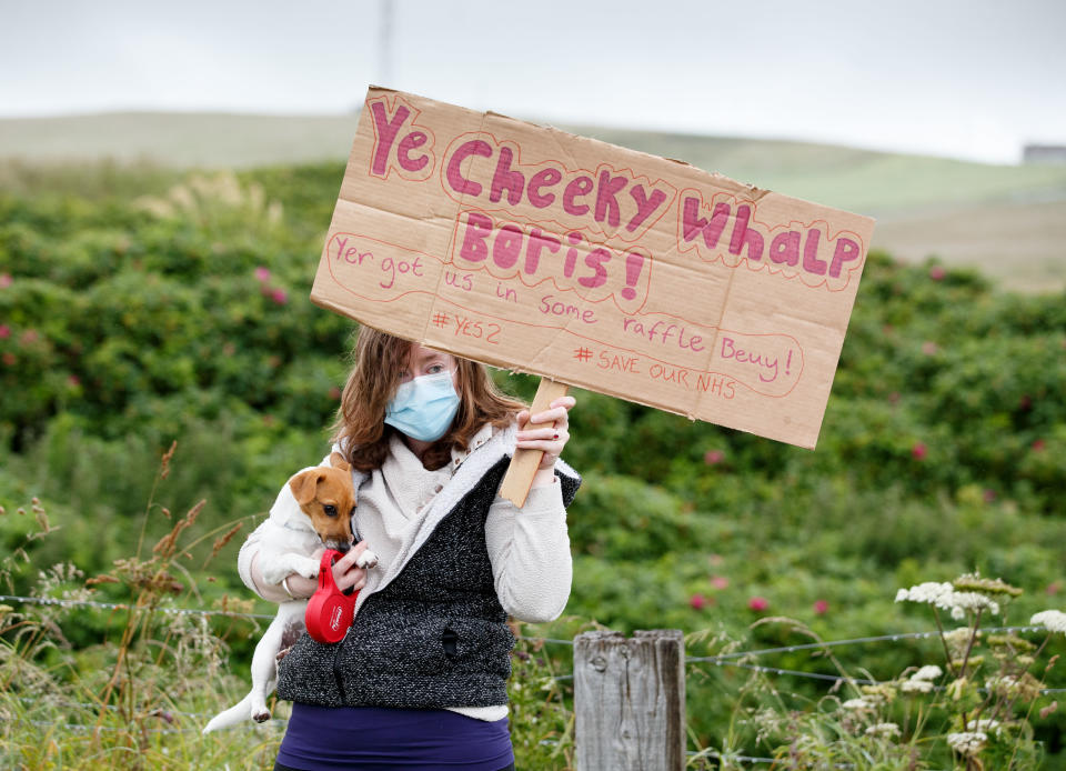 STROMNESS, SCOTLAND - JULY 23: A protester holds her dog and a sign as a group of demonstrators gather to greet British Prime Minister Boris Johnson as he visits the Orkney Islands on July 23, 2020 in Stromness, Scotland. This week marks one year as U.K. Prime Minister for Conservative Party leader Boris Johnson. Today he is visiting businesses in the Orkney Islands in Scotland to reaffirm his commitment to supporting all parts of the UK through the Coronavirus pandemic. Later he will visit a military base in Moray to thank Military personnel for their service. (Photo by Robert Perry/Getty Images)