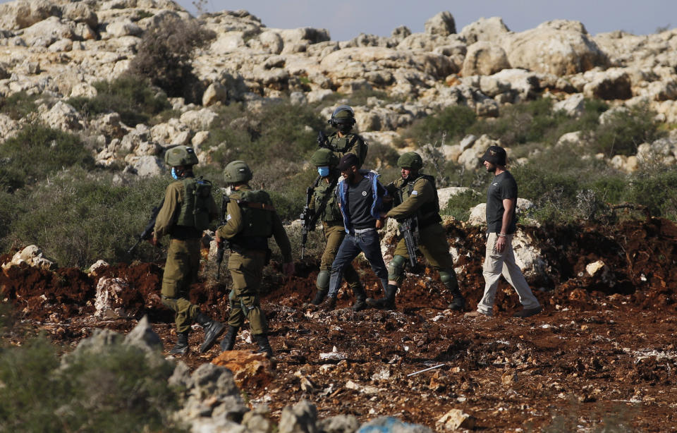 Israeli soldiers arrest a Palestinian during a protest against the expansion of Jewish settlements near the West Bank town of Salfit, Monday, Nov. 30, 2020. In years to come, Israelis will be able to commute into Jerusalem and Tel Aviv from settlements deep inside the West Bank via highways, tunnels and overpasses that cut a wide berth around Palestinian towns. Rights groups say the new roads that are being built will set the stage for explosive settlement growth, even if President-elect Joe Biden's administration somehow convinces Israel to curb its housing construction. (AP Photo/Majdi Mohammed)