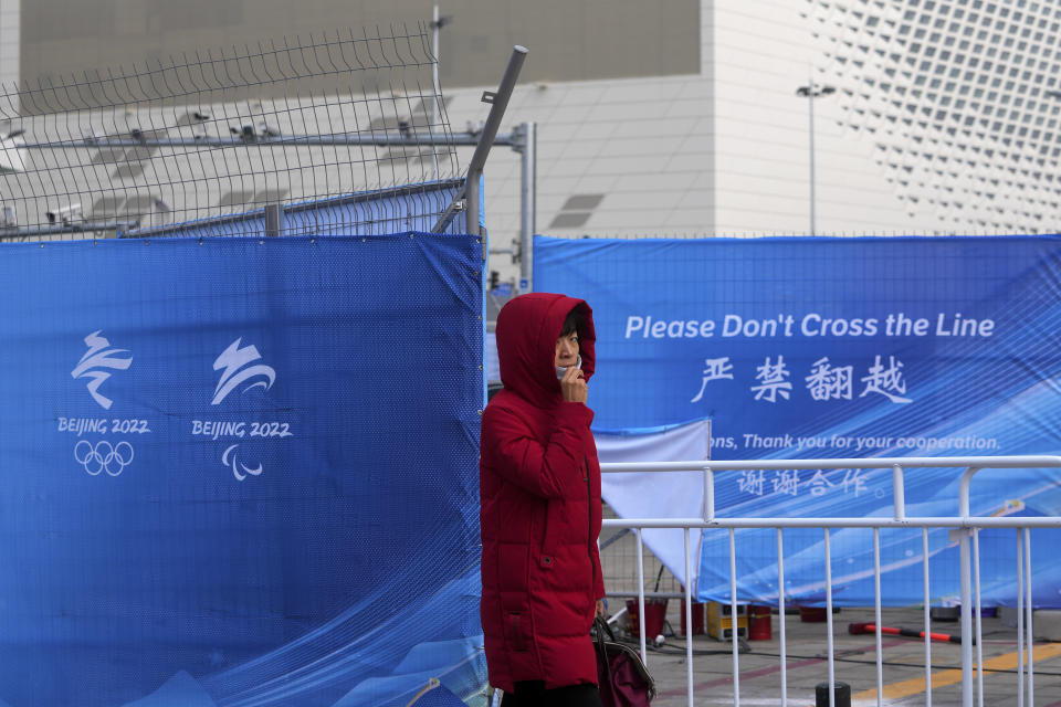 A woman pulls up her face mask to help protect from the coronavirus as she walks by a barricaded area near the Main Press Center (MPC) for the Winter Olympic Games in Beijing, Wednesday, Jan. 19, 2022. China has locked down parts of Beijing's Haidian district following the detection of three cases, just weeks before the capital is to host the Winter Olympic Games. (AP Photo/Andy Wong)