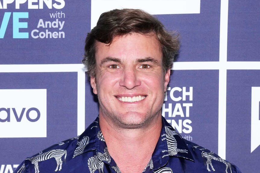 Shep Rose smiling in a navu, zebra patterned, shirt in front of the WWHL step and repeat in New York City.