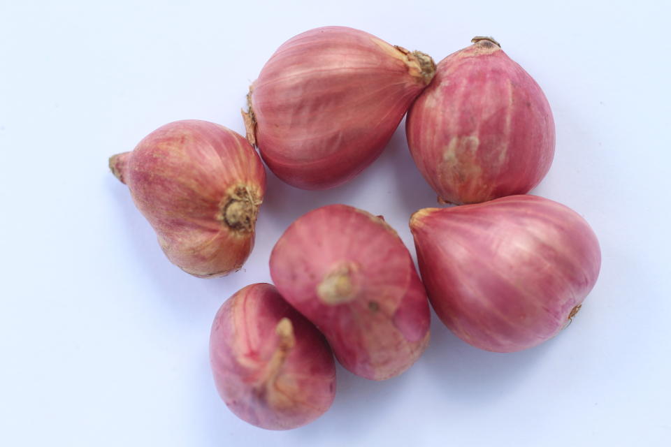 Seven unpeeled shallots on a white surface