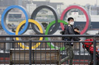People wearing face masks to protect against the spread of the coronavirus walk on the Odaiba waterfront as Olympic rings is seen in the background in Tokyo, Tuesday, Jan. 26, 2021. (AP Photo/Koji Sasahara)
