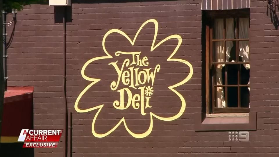 A sign on a building reads "The Yellow Deli" with a decorative flower around it