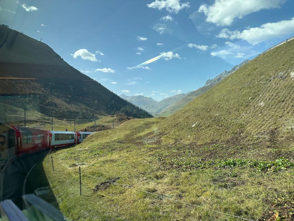 train winding through a green valley viewed through the window of a rear car