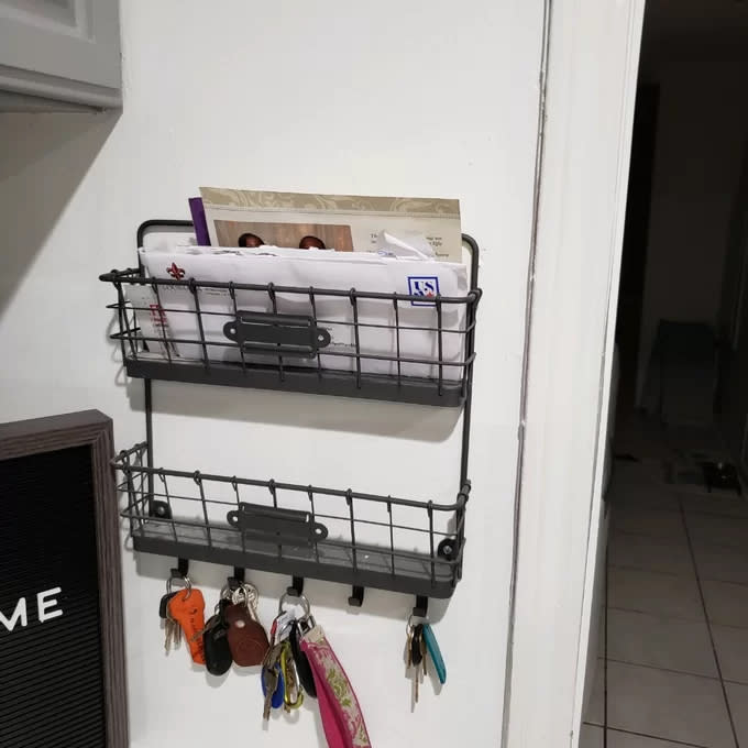 Reviewer's photo of the wall organizer with mail in the top basket, an empty bottom basket, and four sets of keys hanging from five hooks