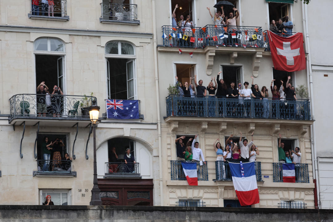 PARIS, FRANCE - JULY 26: Spectators with flags of Australia, France and Switzerland look out from apartments to watch the floating parade on the river Seine during the Opening Ceremony of the Olympic Games Paris 2024 on July 26, 2024 in Paris, France. (Photo by  Nir Elias - Pool/Getty Images)