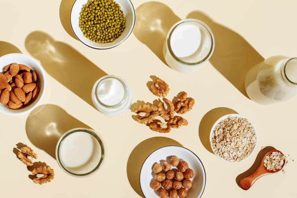 Various organic vegan plant based milk in glasses and glass bottle and ingredients (nuts, oatmeal) on beige background. Non Dairy milk substitute drink, healthy eating. Lactose-free milk in minimal flat lay style. Top view.