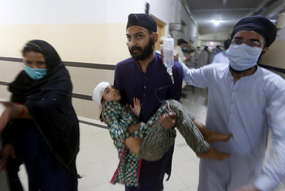 People carry a girl, who was injured in bus and train accident, after receiving initial treatment at a hospital in Sheikhupura near Lahore, Pakistan, Friday, July 3, 2020. A passenger train crashed into a bus carrying Sikh pilgrims at an unmanned railway crossing in eastern Pakistan, police and rescue officials said. (AP Photo/K.M. Chaudary)