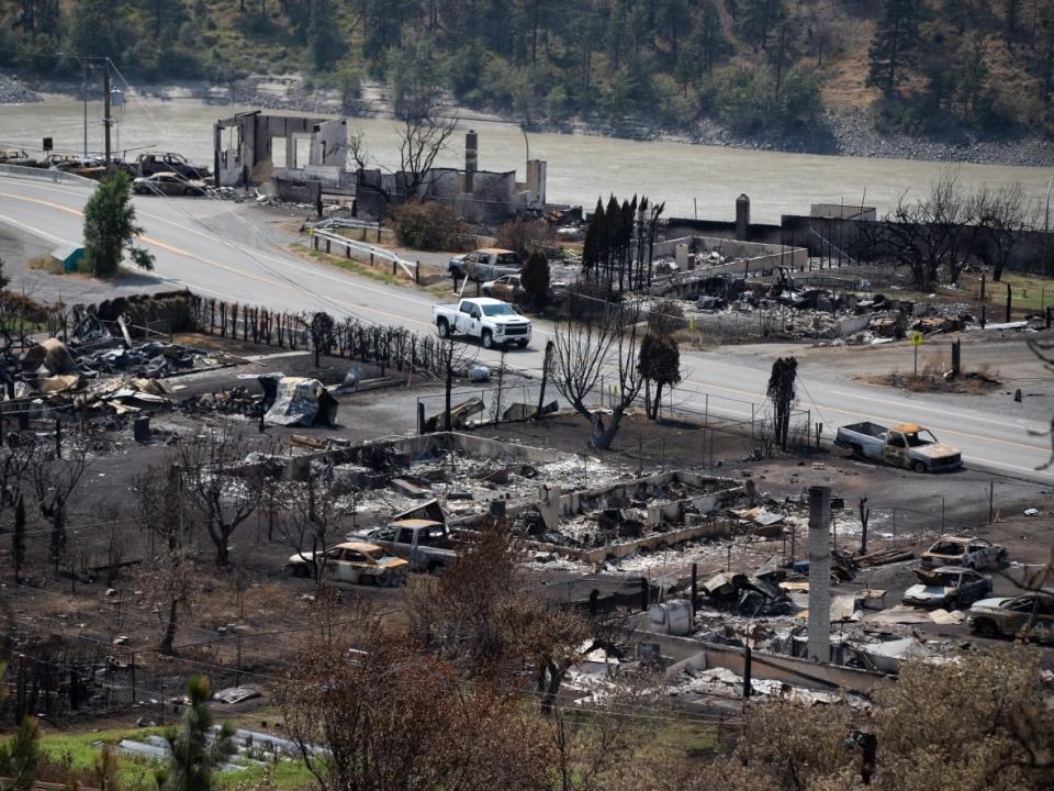 An RCMP vehicle drives past the remains of vehicles and structures in Lytton, B.C., on Friday, July 9, 2021, after a wildfire destroyed most of the village on June 30.  (Darryl Dyck/The Canadian Press - image credit)