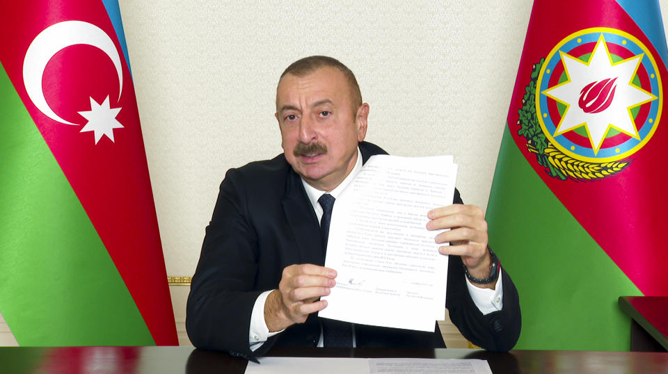 In this handout photo provided Tuesday, Nov. 10, 2020, by the Azerbaijan's Presidential Press Office, showing Azerbaijani President Ilham Aliyev gestures as he shows an agreement while addressing the nation in Baku, Azerbaijan. Armenia and Azerbaijan announced an agreement early Tuesday to halt fighting over the Nagorno-Karabakh region of Azerbaijan under a pact signed with Russia that calls for deployment of nearly 2,000 Russian peacekeepers and territorial concessions. (Azerbaijani Presidential Press Office via AP)