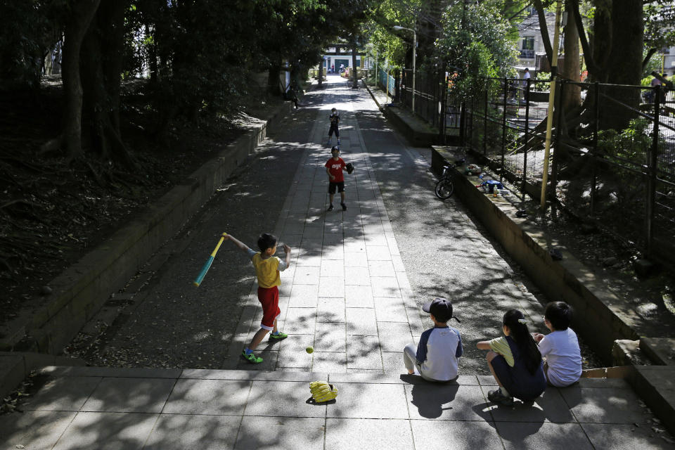 FILE - In this April 19, 2020, file photo, children, some wearing protective masks to prevent the spread of the coronavirus, play baseball on a walkway to Shibuya Hikawa-Jijja shinto shrine in Tokyo. Under Japan's coronavirus state of emergency, people have been asked to stay home. Many are not. Some still have to commute to their jobs despite risks of infection, while others are dining out, picnicking in parks and crowding into grocery stores with scant regard for social distancing. (AP Photo/Kiichiro Sato, File)