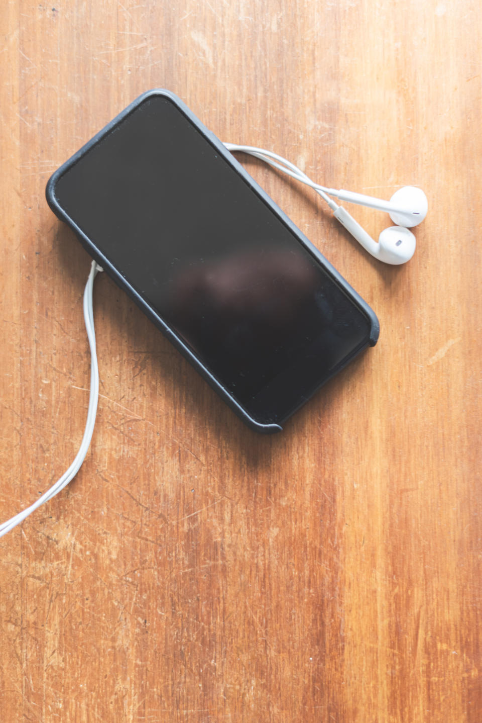 Smartphone with earbuds on a wooden surface, illustrating work or financial planning with tech