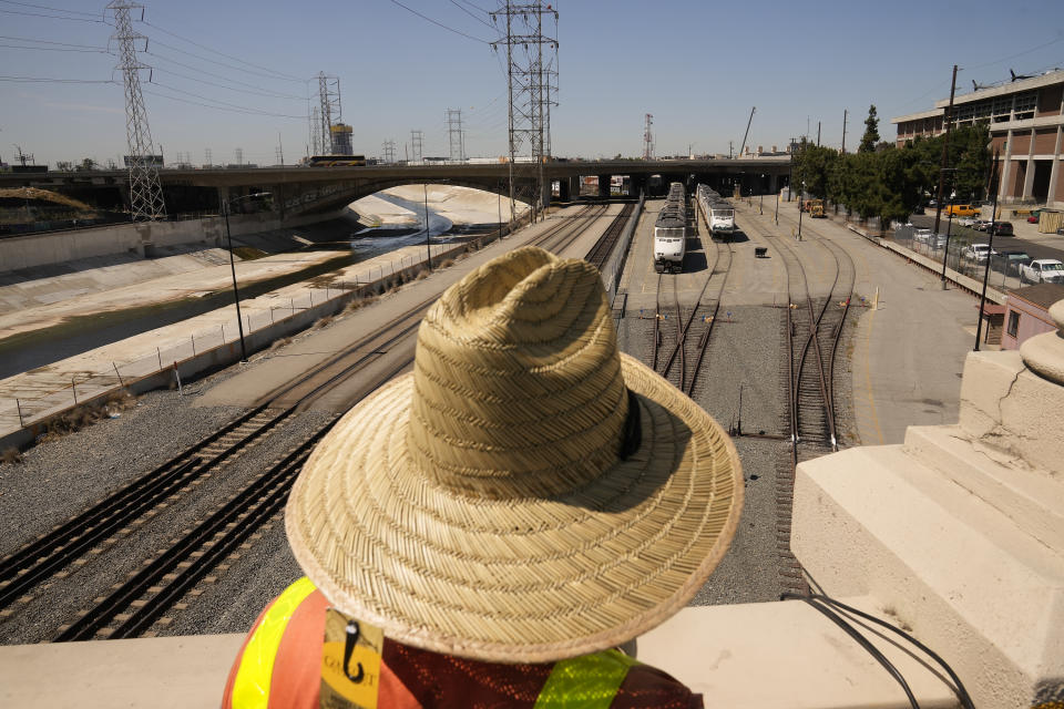 Electrician David Guerrero, with IBEW Local 11, pulls out an old copper cable line under excessive heat from the old Cesar Chavez Avenue Viaduct at the in Los Angeles, Thursday, July 13, 2023. The Los Angeles River is seen bottom left. After a historically wet winter and a cloudy spring, California's summer was in full swing Thursday as a heat wave that's been scorching much of the U.S. Southwest brings triple digit temperatures and an increased risk of wildfires. (AP Photo/Damian Dovarganes)