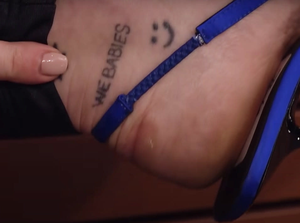 the words "we babies" on Miley's ankle in all caps above a smiley face tattoo