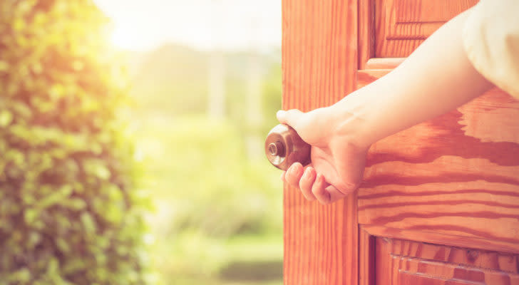 hand opening a wooden door to the outdoors. represents economic reopening