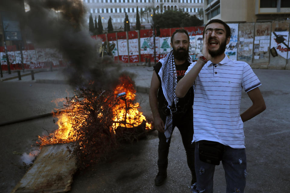 An anti-government protester chants slogans as others burn tires and woods during a protest against the political leadership they blame for the economic and financial crisis, in front of the government house in downtown Beirut, Lebanon, Thursday, June 11, 2020. (AP Photo/Hussein Malla)