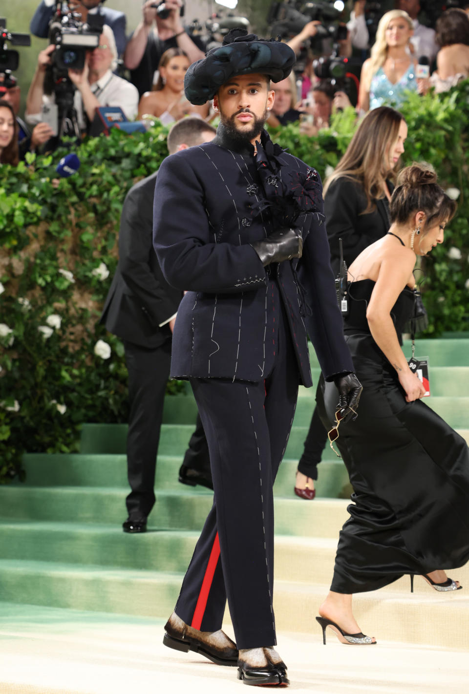 Bad Bunny in an embellished navy suit with matching hat posing on Met Gala steps