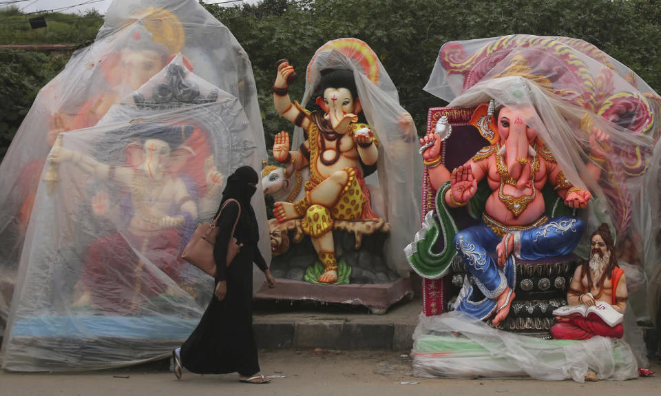 Muslim woman walks past a row of idols