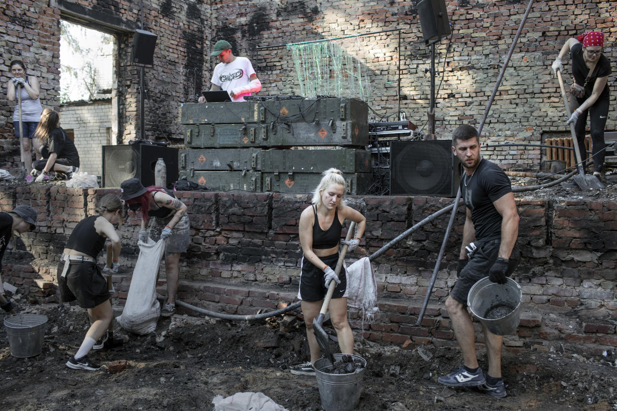 Voluntarios reunidos por el grupo activista Repair Together trabajan para limpiar los escombros de las ruinas de un edificio bombardeado y dañado por la guerra mientras un DJ toca en Yahidne, Ucrania, el 23 de julio de 2022. (Emile Ducke/The New York Times)