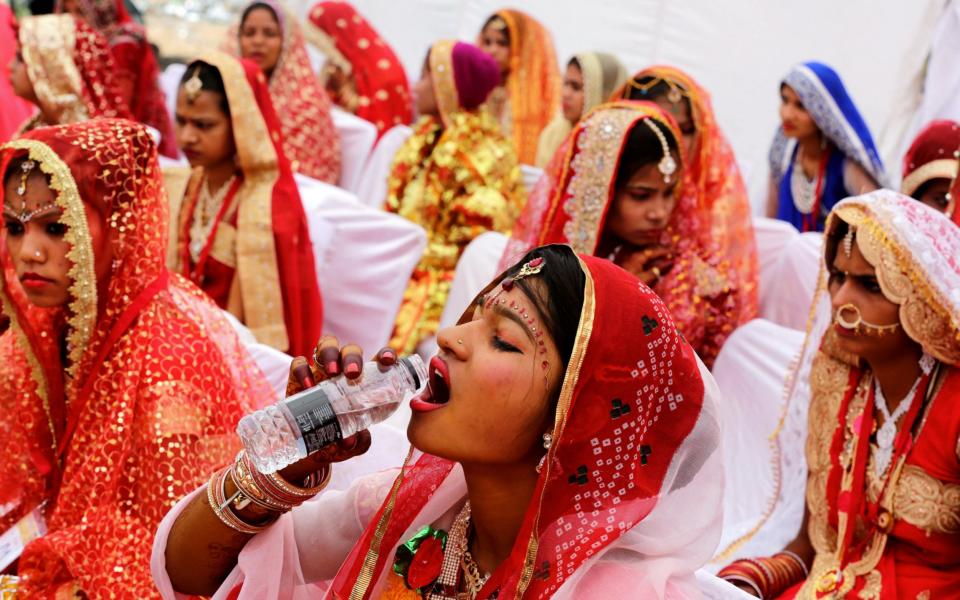 An Indian bride drinks water as she sits with other brides during a mass marriage ceremony - Credit: SANJEEV GUPTA / EPA