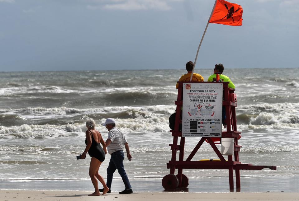 Beachgoers walk past a couple of Volusia County Beach Safety Ocean Rescue lifeguards in May as a rough surf keeps most visitors out of the water near the Daytona Pier. With big crowds expected to head to the beach on July 4th weekend, there is still a shortage of lifeguards to watch over them.