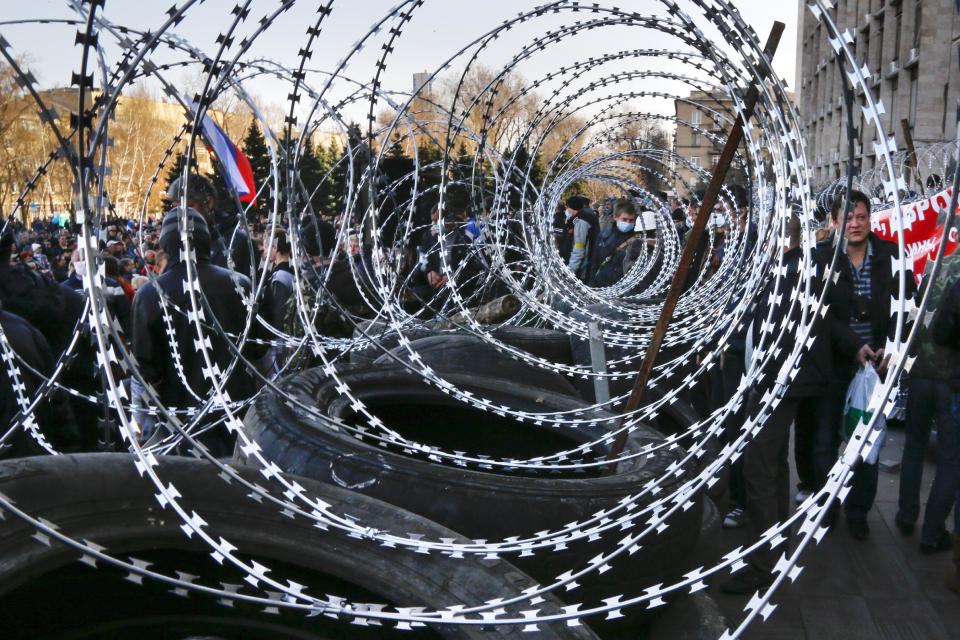 People gathered near of a barricade with razor wires at the regional administration building in Donetsk, Ukraine, Monday, April 7, 2014. Outside the Donetsk building, a barricade of car tires and razor wire was built up to thwart police from retaking it. Interfax cited police in Donetsk as saying one armed group fired into the air and attempted to seize the regional state television broadcaster Monday but retreated after police and guards in the building also fired warning shots into the air. (AP Photo/Andrey Basevych)