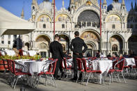 FILE - In this Friday, Feb. 28, 2020 file photo, two waiters wait for customers in a restaurant at St. Mark's Square in Venice, Italy. With the coronavirus emergency deepening in Europe, Italy, a focal point in the contagion, risks falling back into recession as foreign tourists are spooked from visiting its cultural treasures and the global market shrinks for prized artisanal products, from fashion to design. (Claudio Furlan/Lapresse via AP, File)