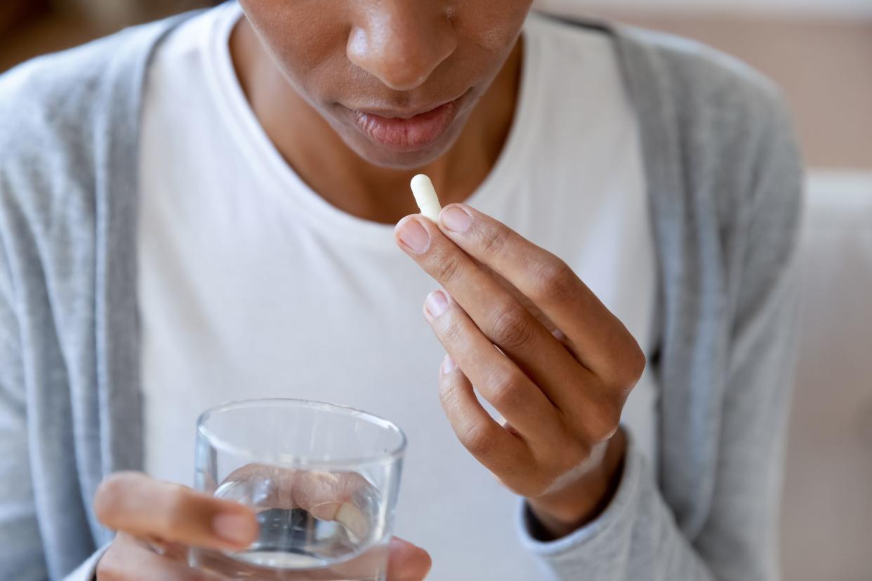 Close up of African American young woman feel sick drink antibiotic or antidepressant pill with water, biracial female suffer from illness take prescribed medicines or tablet, healthcare concept