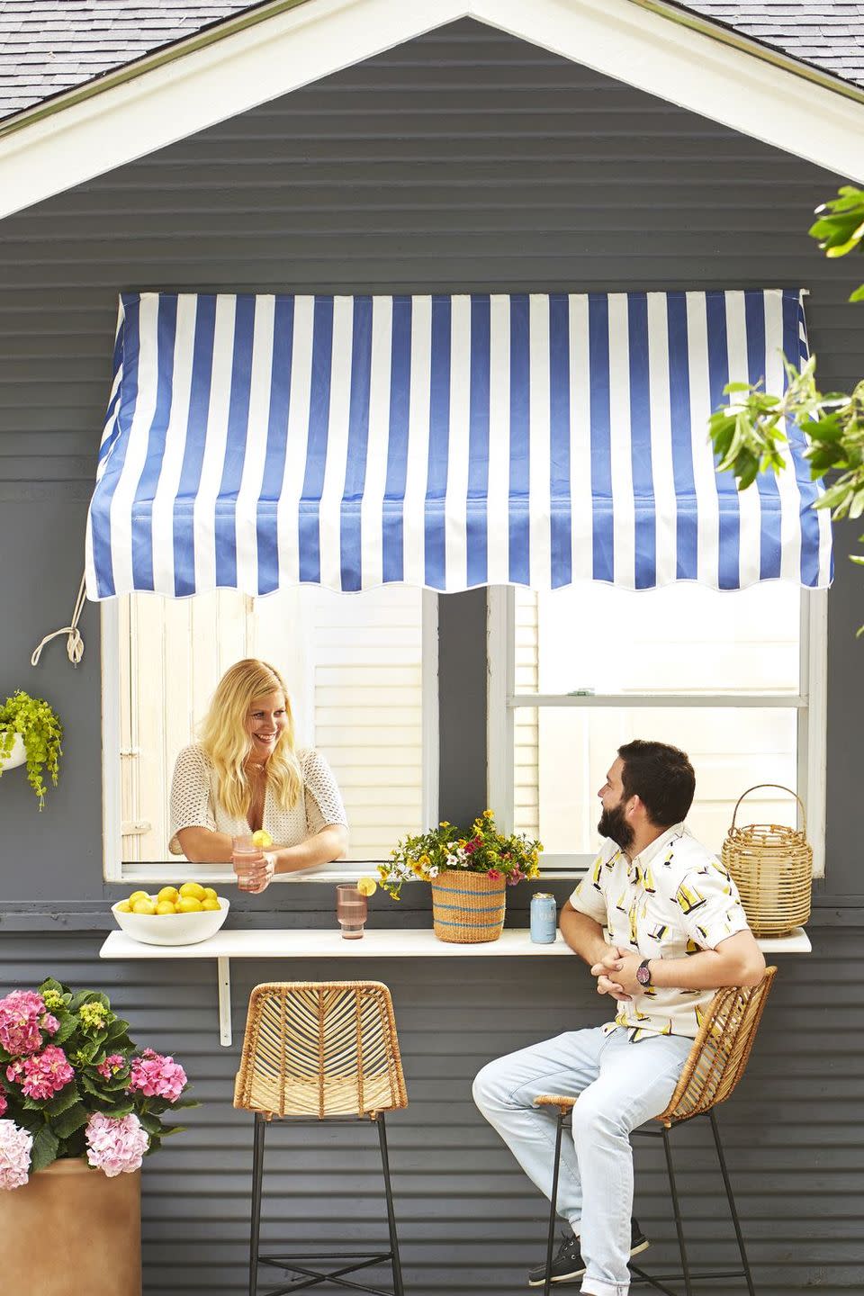 <p>Keep party guests out of the kitchen with this DIY serving station. Simply install a serving ledge under a window and dress the space with weather-resistant bar stools and a patterned awning. </p>