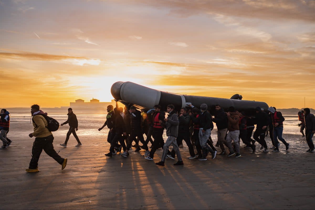 Migrants carry a smuggling boat on their shoulders as they prepare to embark on the beach of Gravelines, near Dunkirk, northern France on October 12, 2022 (AFP via Getty Images)