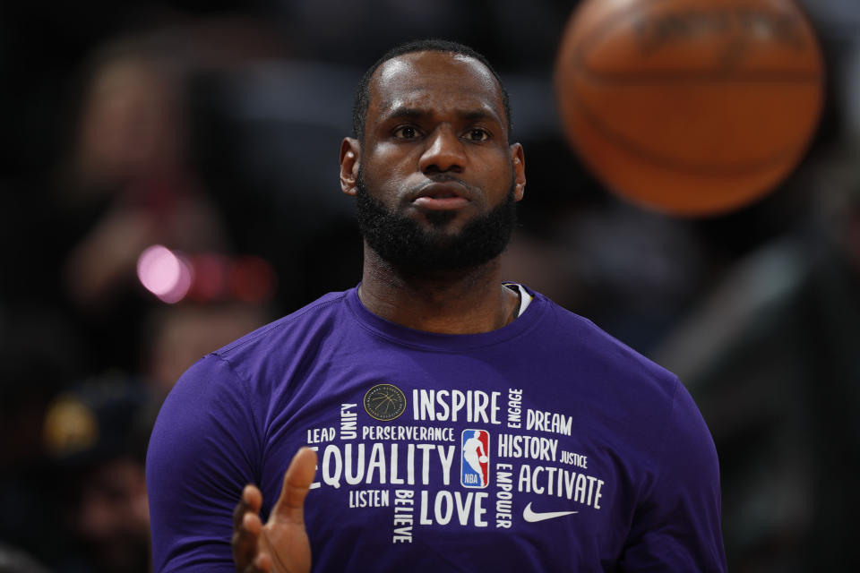 LeBron James, in a purple shirt with sayings such as "inspire, equality, love, activate" prepares to catch a basketball.