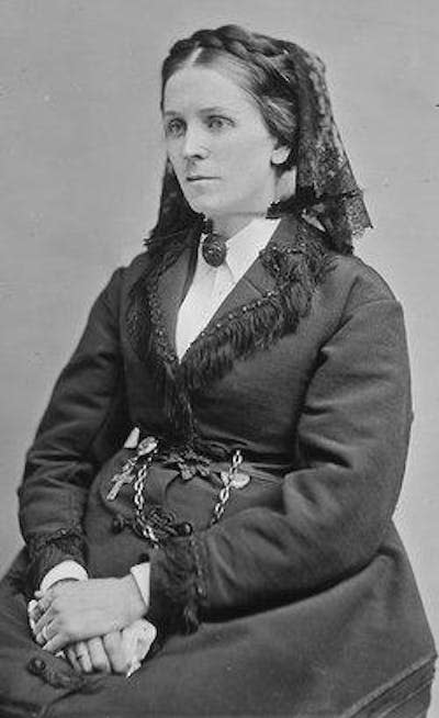 A black and white portrait of a seated woman in a heavy black dress.