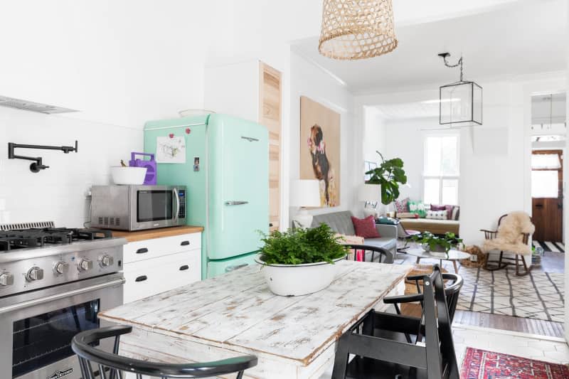 A whitewashed rustic wood dining table in a vintage-inspired kitchen with a mint green fridge