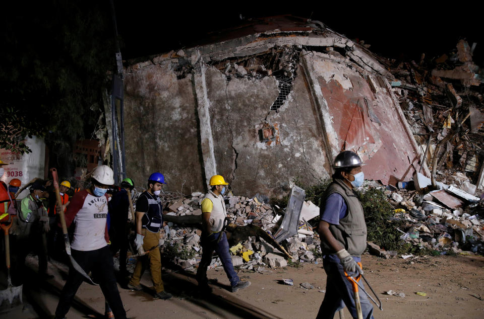 Workers walk past a collapsed building.&nbsp;