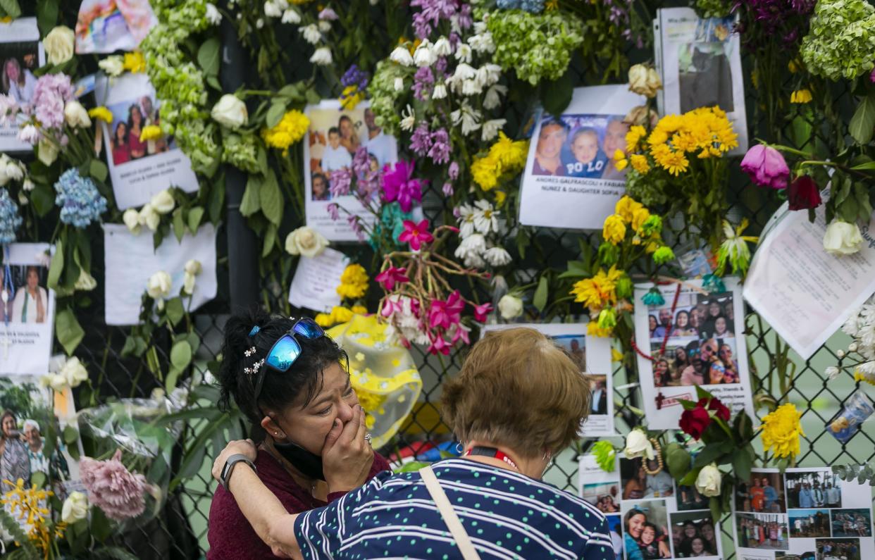 In this June 29, 2021, photo, mourners visit a makeshift memorial near the site of the collapsed condominium in Surfside, Fla. While hundreds of rescuers search desperately for survivors within the rubble of the collapsed condominium, a smaller cadre of mental health counselors are also deploying to help families and other loved ones cope with the tragedy.