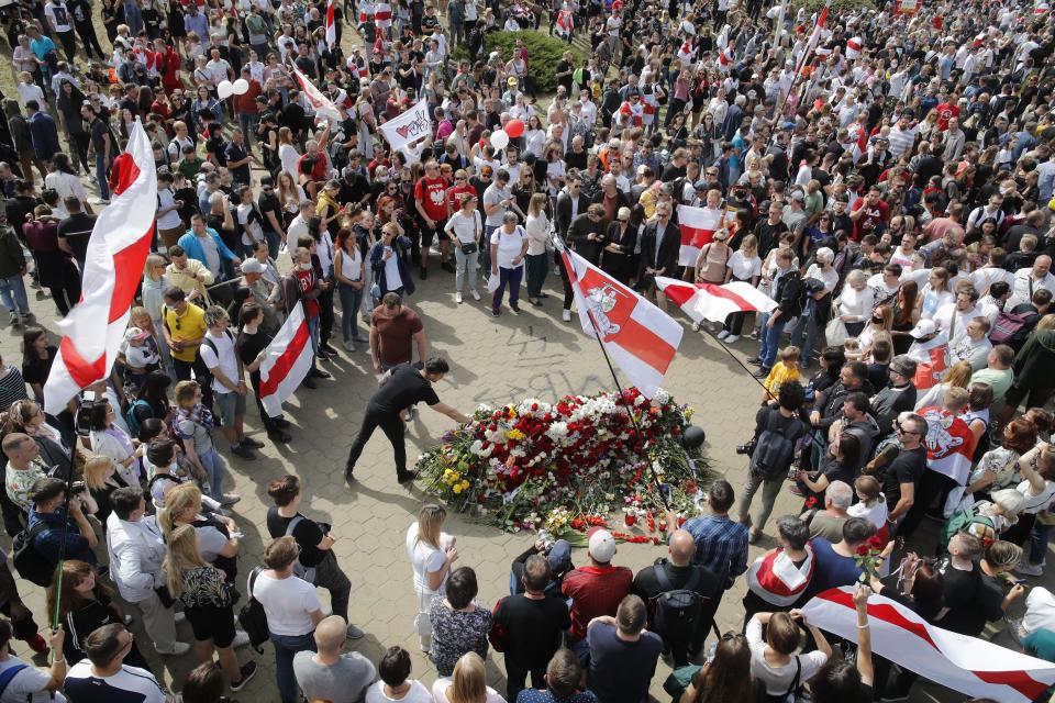 People with old Belarusian National flags lay flowers as they gather at the place where Alexander Taraikovsky died amid the clashes protesting the election results, during his civil funeral in Minsk, Belarus, Saturday, Aug. 15, 2020. Taraikovsky died Monday as demonstrators roiled the streets of the capital Minsk, denouncing official figures showing that authoritarian President Alexander Lukashenko, in power since 1994, had won a sixth term in office. (AP Photo/Dmitri Lovetsky)