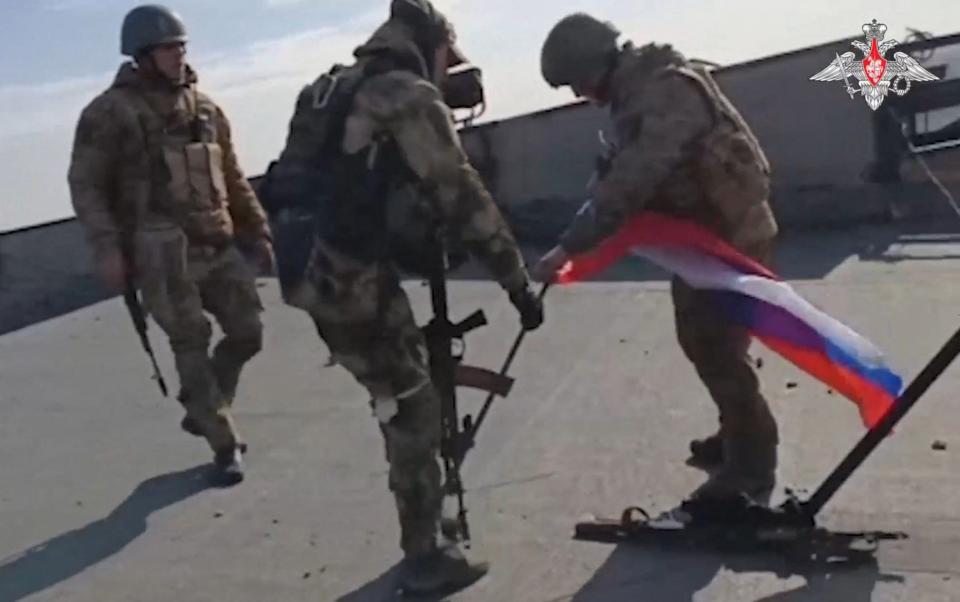 Russian soldiers place a Russian national flag on the rooftop of the Avdiivka Coke and Chemical Plant